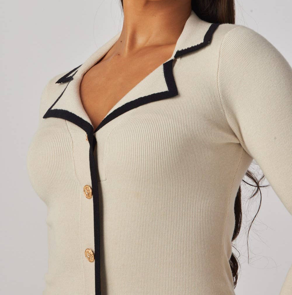 Woman wearing a cream-colored cardigan with black trim on a plain background